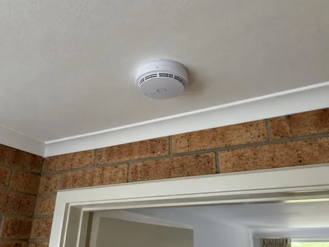 Ceiling-mounted smoke alarm above a doorway in a brick wall home interior in Tuggerah