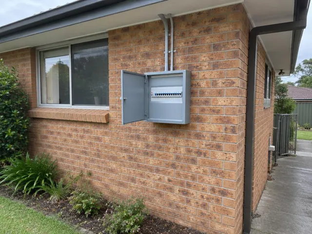 Open electrical switchboard on a brick exterior wall beside a window in Niagara Park